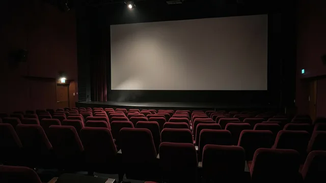 Imagem gerada por IA: Sala de cinema vazia diante de uma tela iluminada.