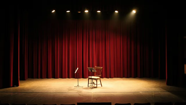 Imagem gerada por IA: Palco de ópera vazio, iluminado por luzes quentes diante de cortinas vermelhas.