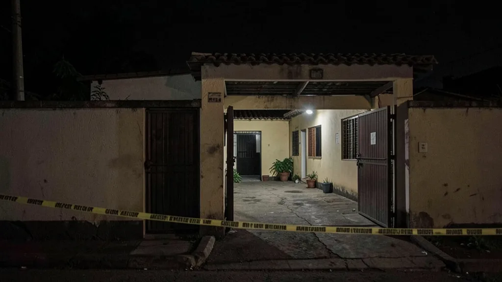 Imagem gerada por IA: Fachada de uma residência no Recife à noite, com fita policial diante do portão.