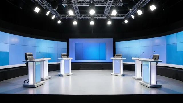 Palco vazio de debate presidencial em um estúdio de televisão, com púlpitos sob iluminação de estúdio.