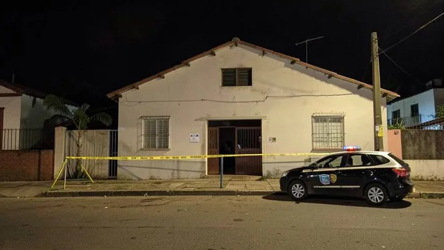 Imagem gerada por IA: Fachada de uma igreja em um bairro residencial à noite, com viatura policial próxima à entrada.