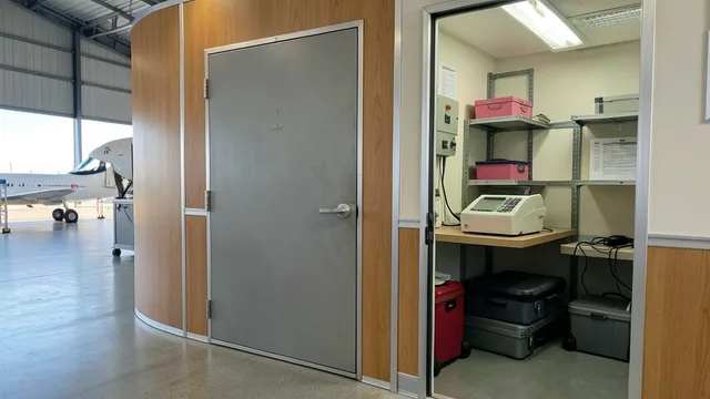 Imagem gerada por IA: Porta metálica escondida atrás de uma divisória de madeira em um hangar.