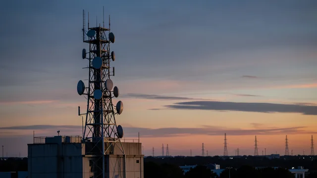 Imagem gerada por IA: Torre de telefonia com antenas e equipamentos de comunicação ao entardecer.