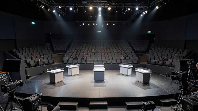 Palco vazio de debate presidencial em estúdio de televisão, com púlpitos sob iluminação de estúdio.
