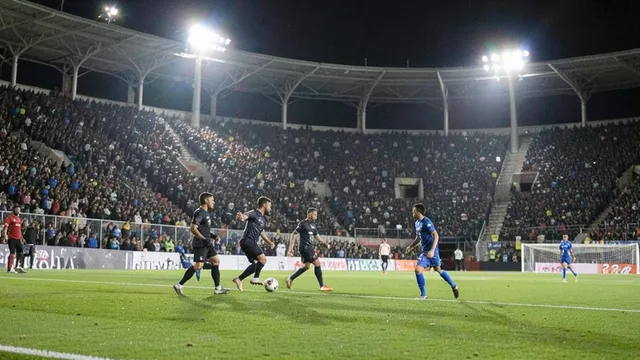 Imagem gerada por IA: Partida de futebol à noite em um estádio lotado, com jogadores disputando a bola sob refletores.